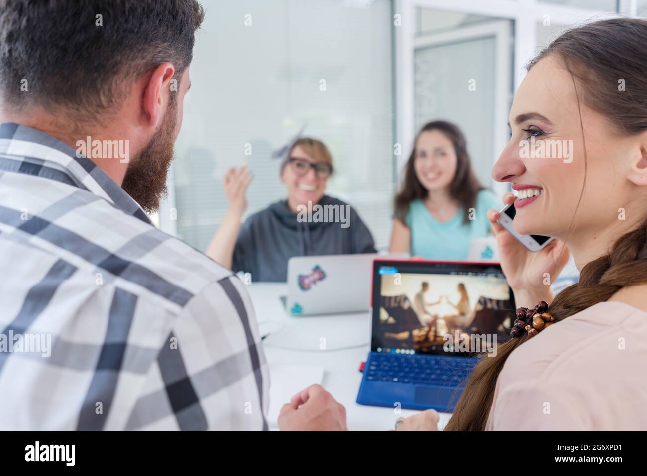 Seitenansicht eines kreativen weiblichen Freiberufler lächelnd zu ihr Mitarbeiter, während Sie einen Anruf auf dem Mobiltelefon in einem gemeinsamen Schreibtisch in entspannter Arbeiten environ Stockfoto