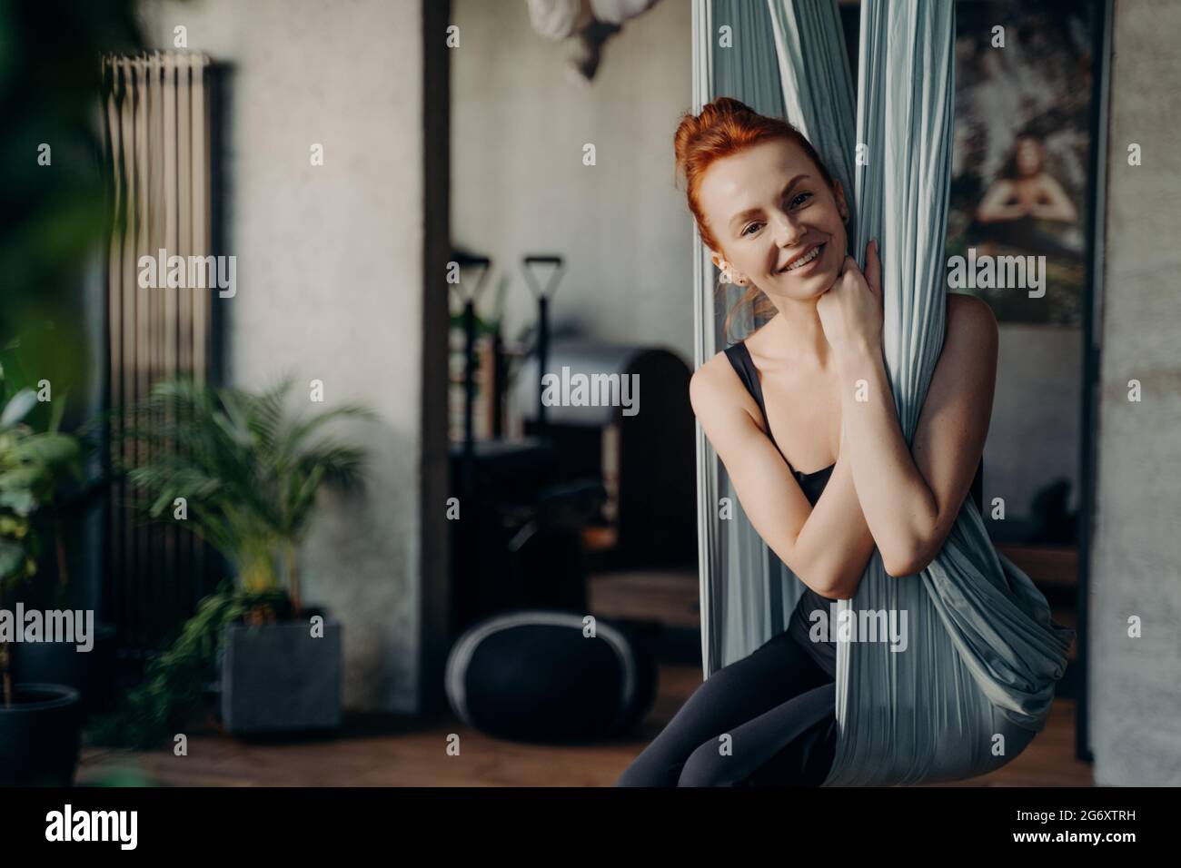 Glückliche rothaarige Frau, die in bequemer Position in der Yogamatte sitzt Stockfoto