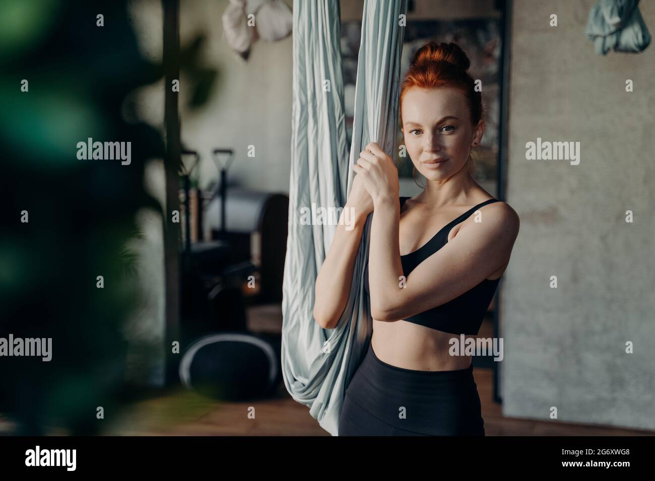 Junge Frau, die im Studio für Antigravitationsyogaübungen bereit ist und in die Kamera schaut Stockfoto