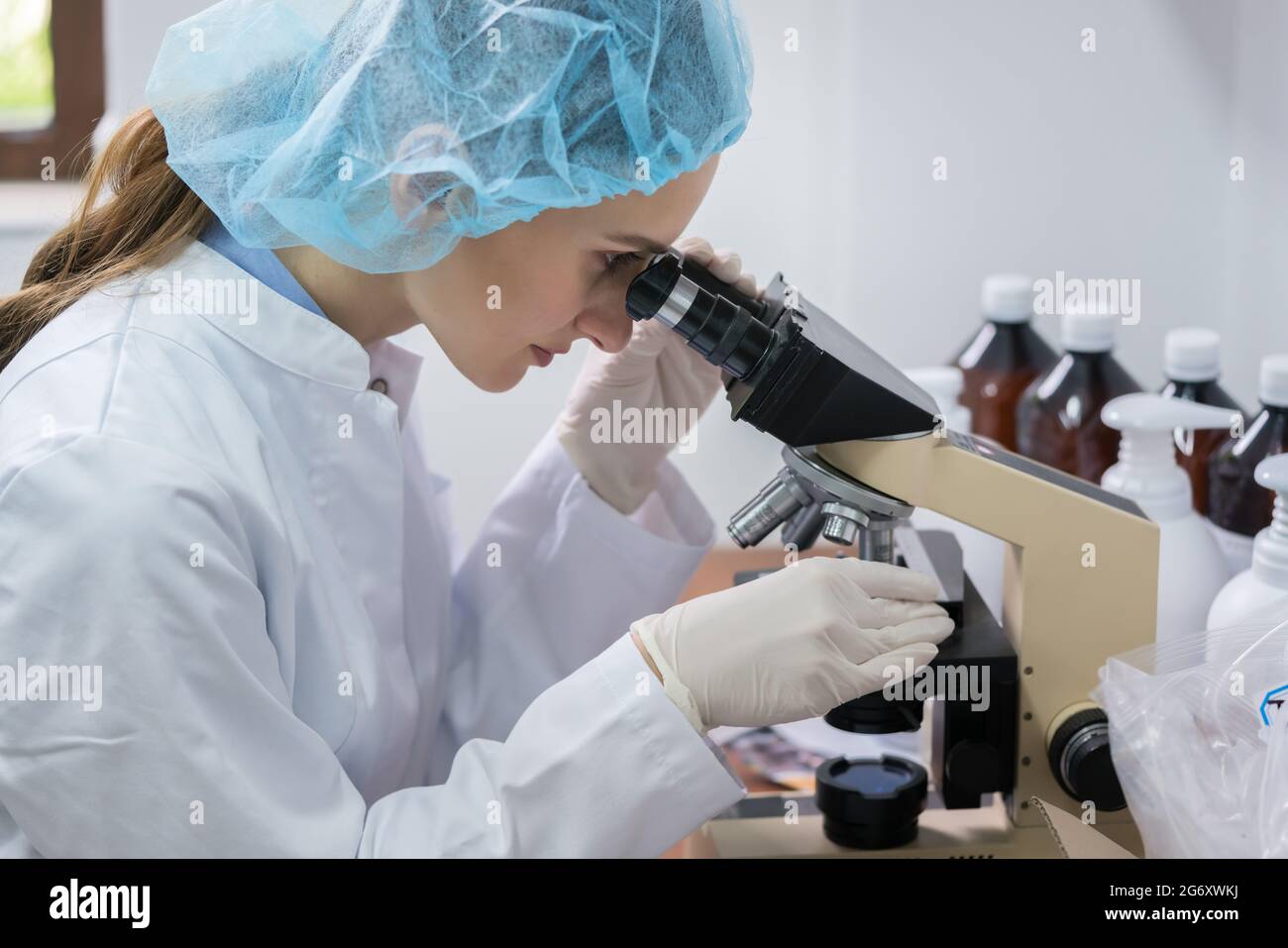 Seitenansicht eines weiblichen Chemiker das Tragen steriler Ausrüstung beim Analysieren Probe unter dem Mikroskop Während der Arbeit im Labor eines kosmetischen Stockfoto