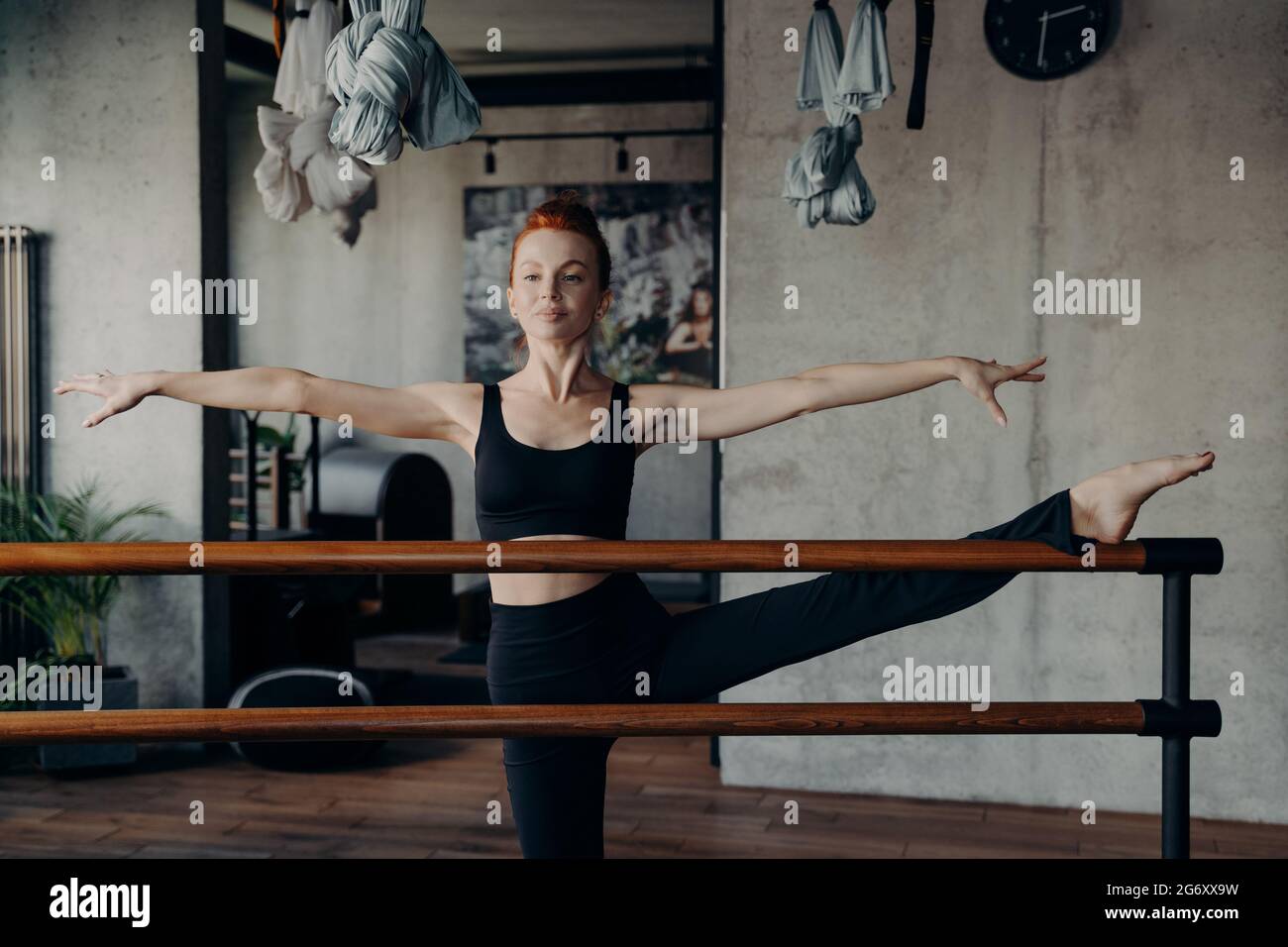 Junge attraktive Frau mit perfekter Körperform Stretching auf Ballettkarre während des Trainings im Fitnessstudio Stockfoto