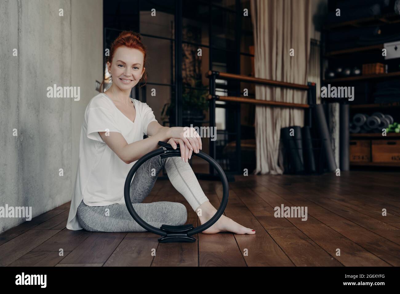 Lächelnde junge sportliche Frau mit Pilates-Ring genießt das Training im Fitnessstudio Stockfoto