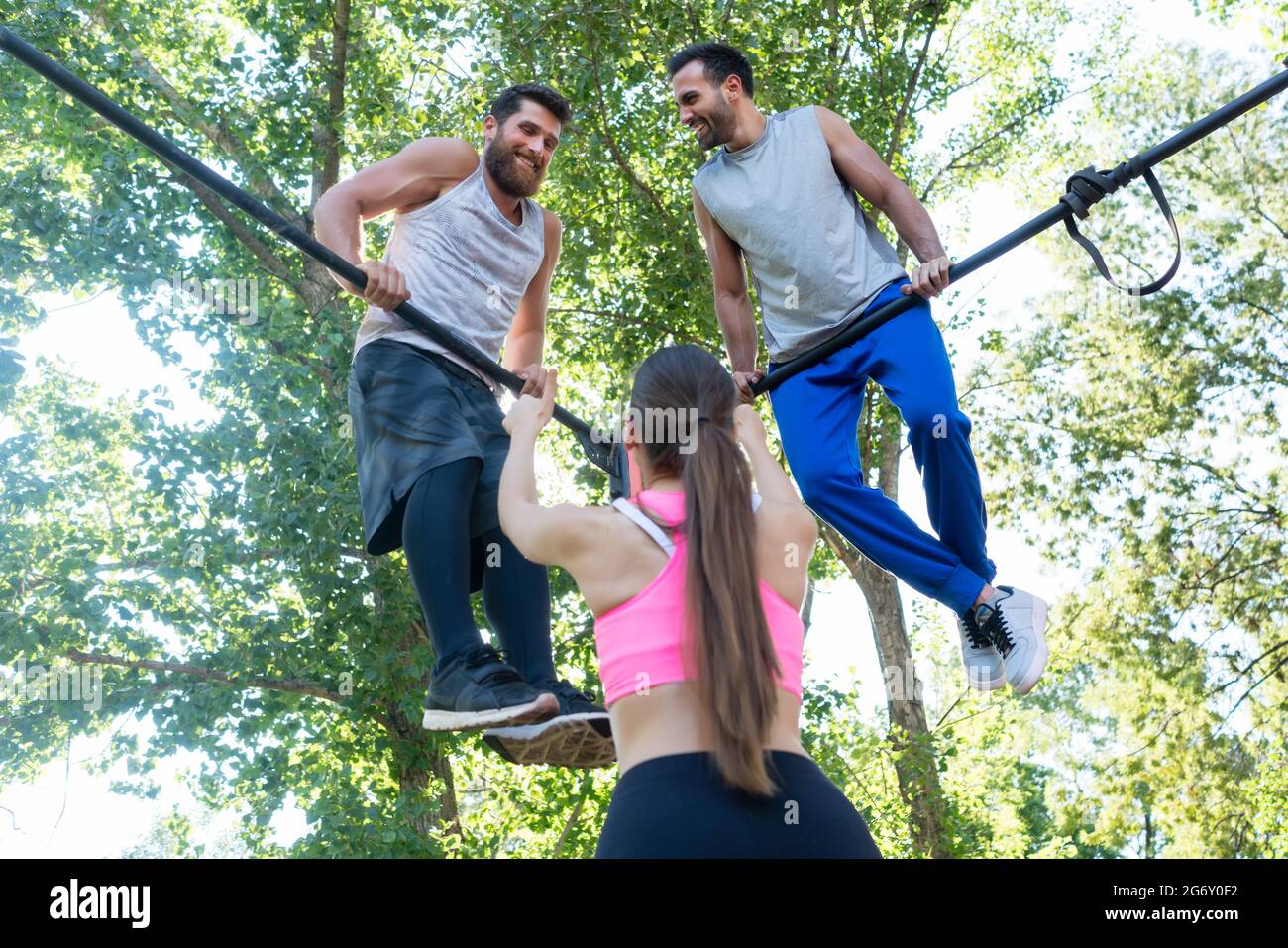 In der Rückansicht zeigt eine fittige Frau, die ihren beiden männlichen Freunden beim extremen Training im Freien in einem modernen Calisthenics-Park den Daumen hoch zeigt Stockfoto