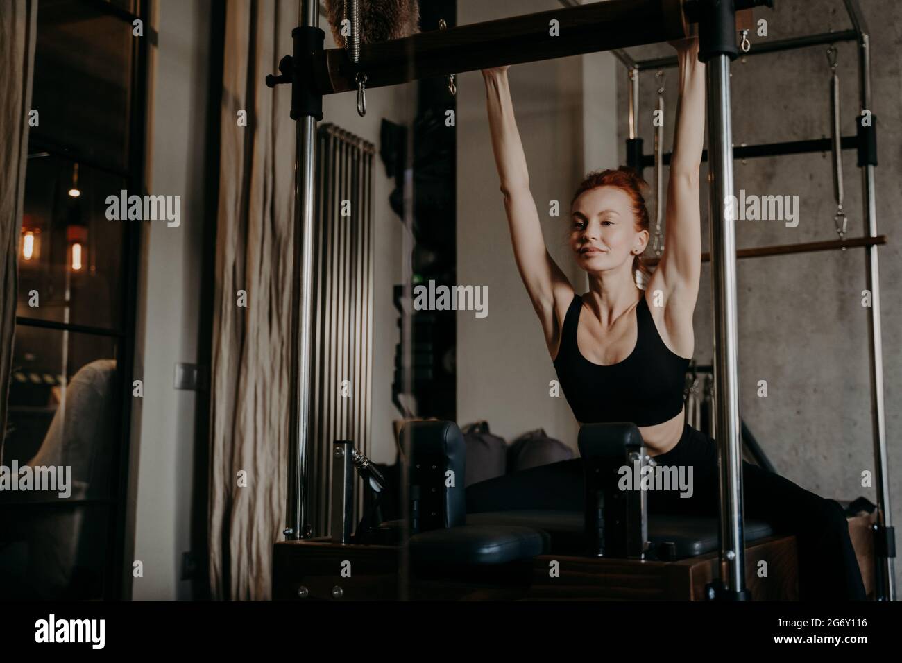 Schöne junge Ingwer Frau tut Oberkörper Stretching Übung auf Reformer Stockfoto