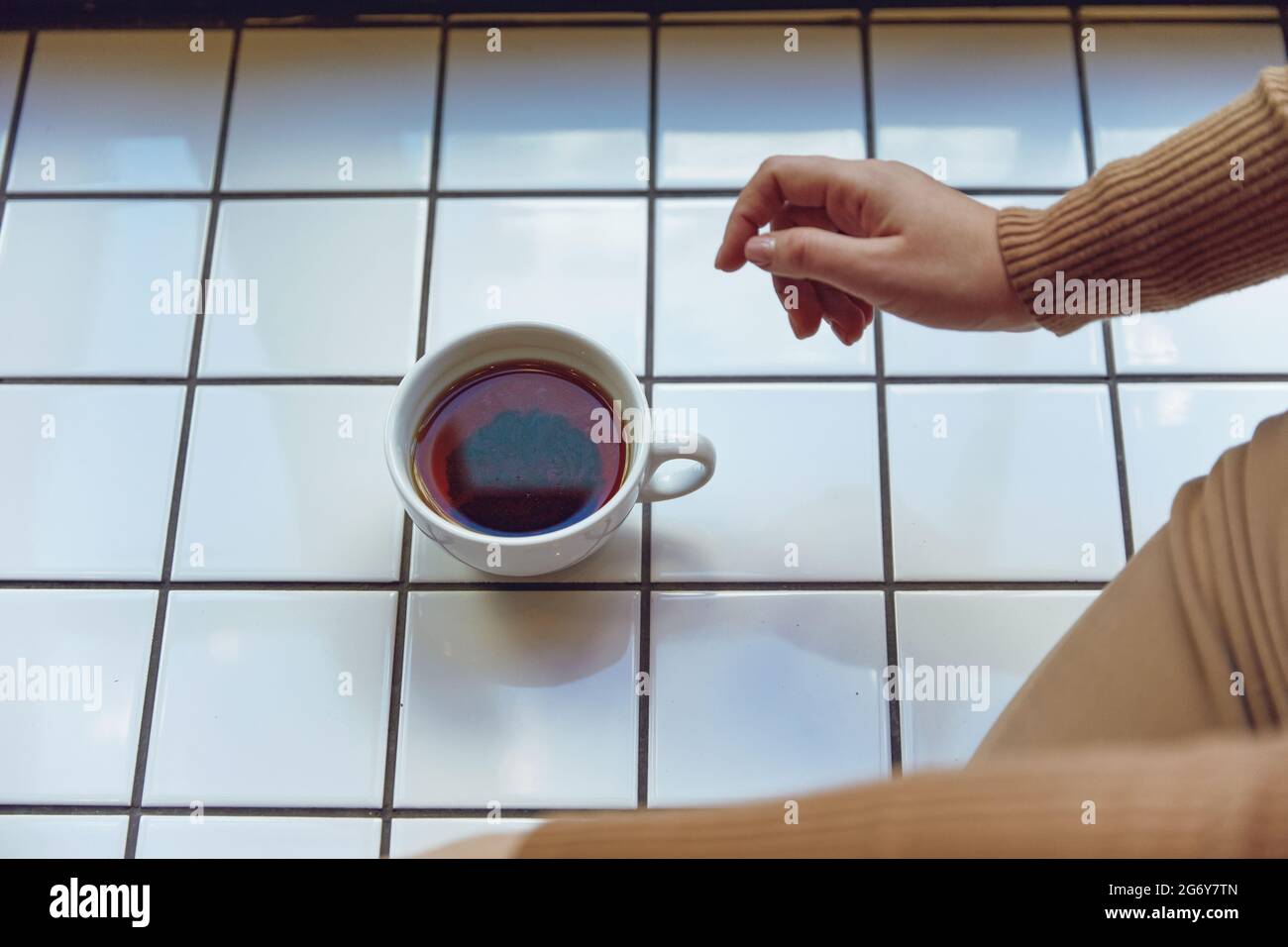 Nahaufnahme einer Frau, die mit einer Tasse Tee auf dem Fensterbrett sitzt Stockfoto