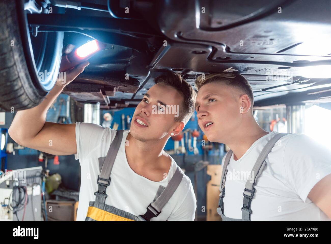 Zwei erfahrene Automechaniker analysieren zusammen die Felgen eines angehobenen Autos, während sie in einer modernen Kfz-Werkstatt arbeiten Stockfoto