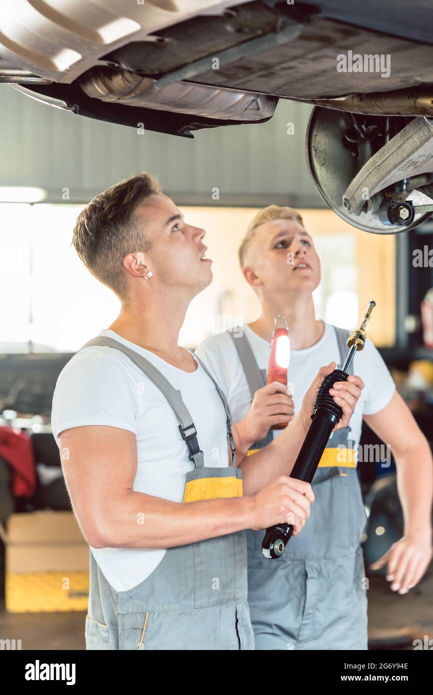 Seitenansicht eines qualifizierten Automechaniker Austausch der Stoßdämpfer eines aufgehoben, während sie gemeinsam mit seinen Kollegen in einem modernen Automobil r Stockfoto