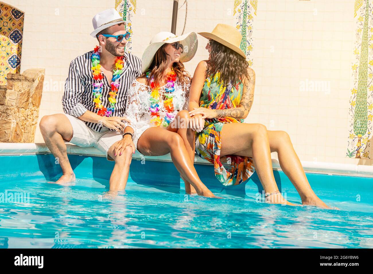 Drei junge Leute lächeln am Rand eines Swimmingpools Stockfoto