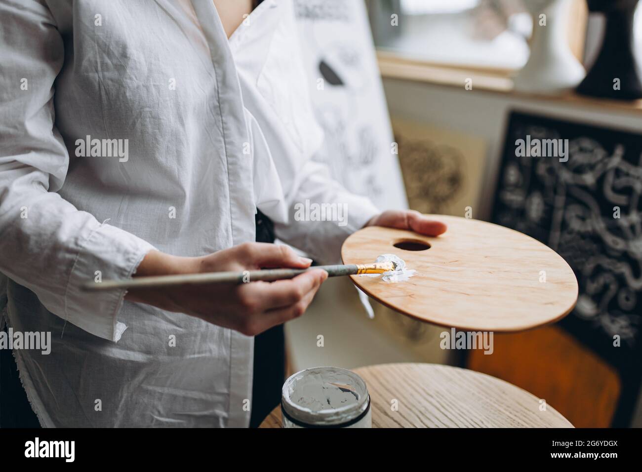 Frau, die weiße Farbe auf Holzkunstpalette mischt Stockfoto