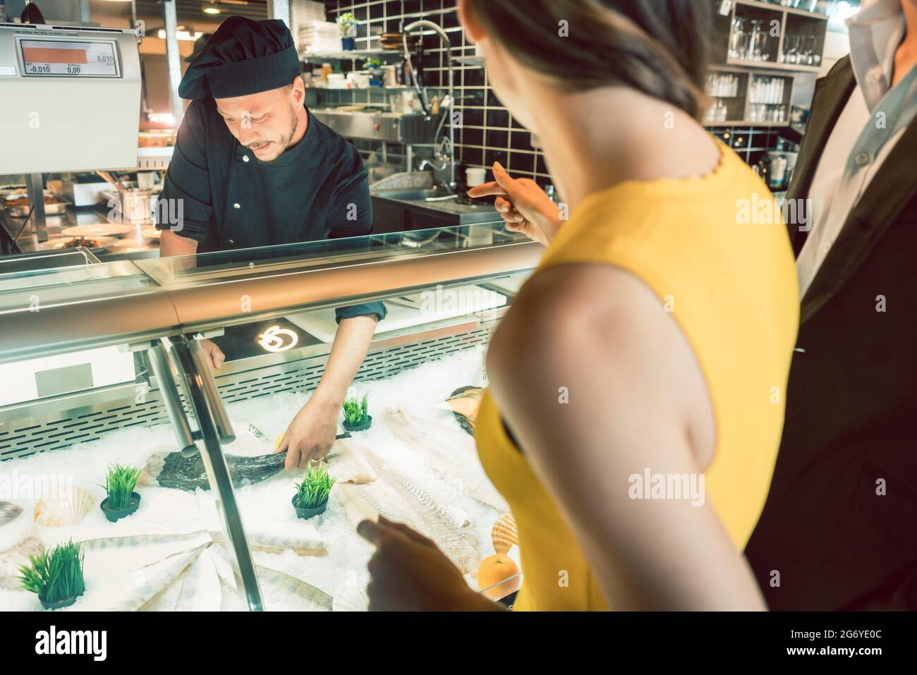 Der erfahrene Meisterkoch nimmt einen frischen Fisch aus dem Gefrierschrank, um ihn für eine Kundin und ihren Partner in einem trendigen Restaurant zu kochen Stockfoto