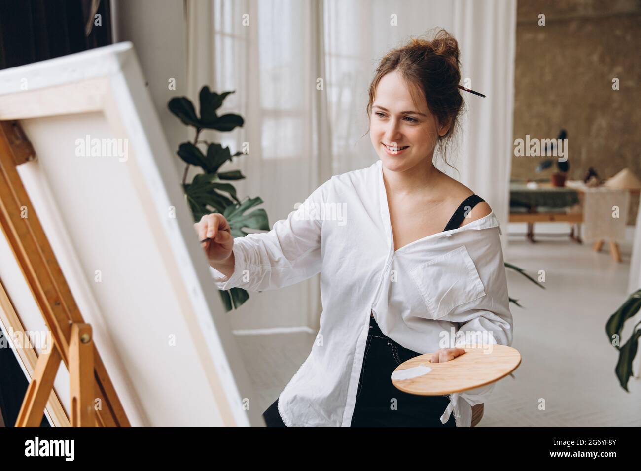 Entzückende Dame beim Zeichnen auf Staffelei im Studio Stockfoto
