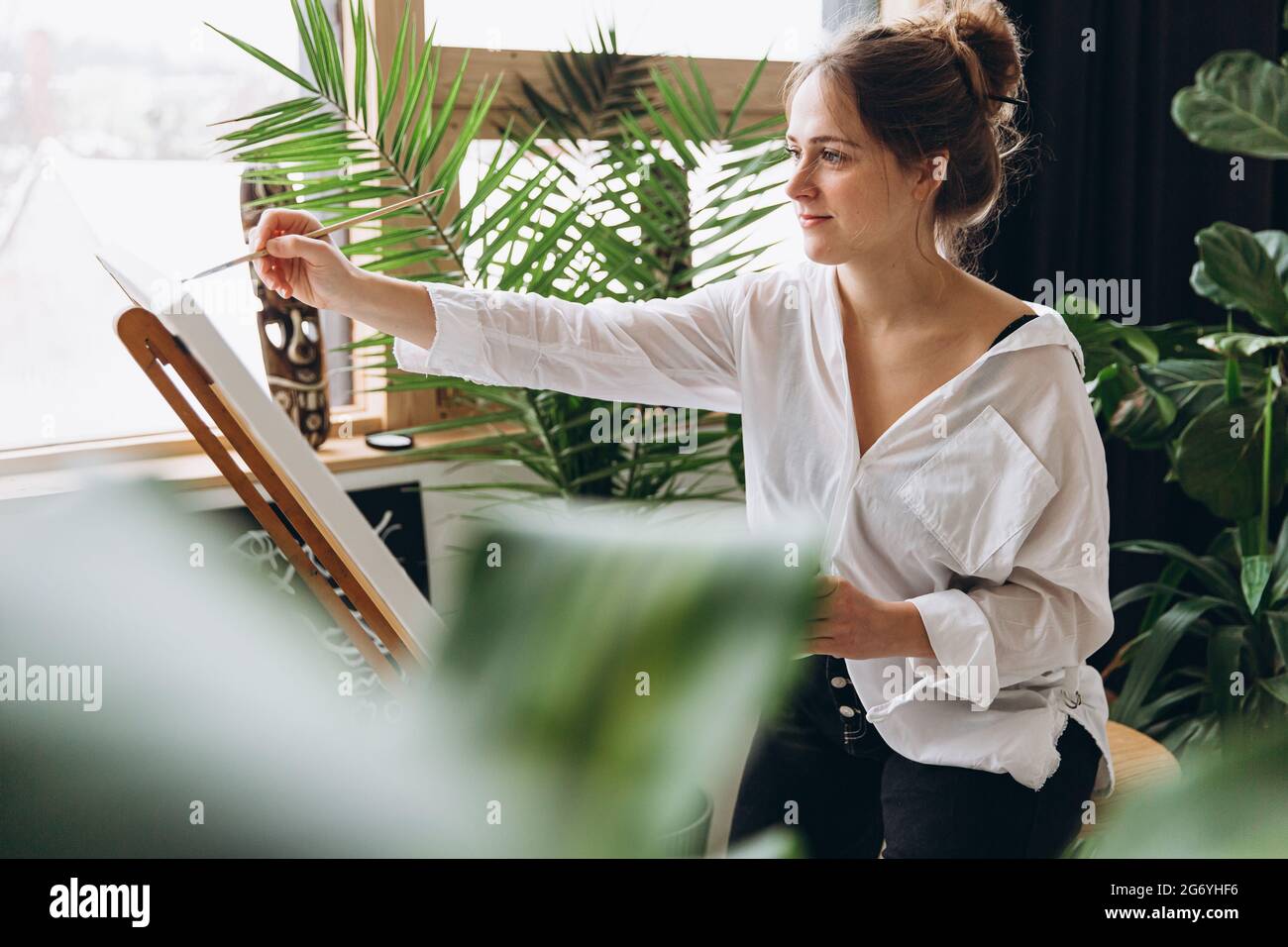 Fokussierte Frau Malerei mit Pinsel auf Staffelei Stockfoto