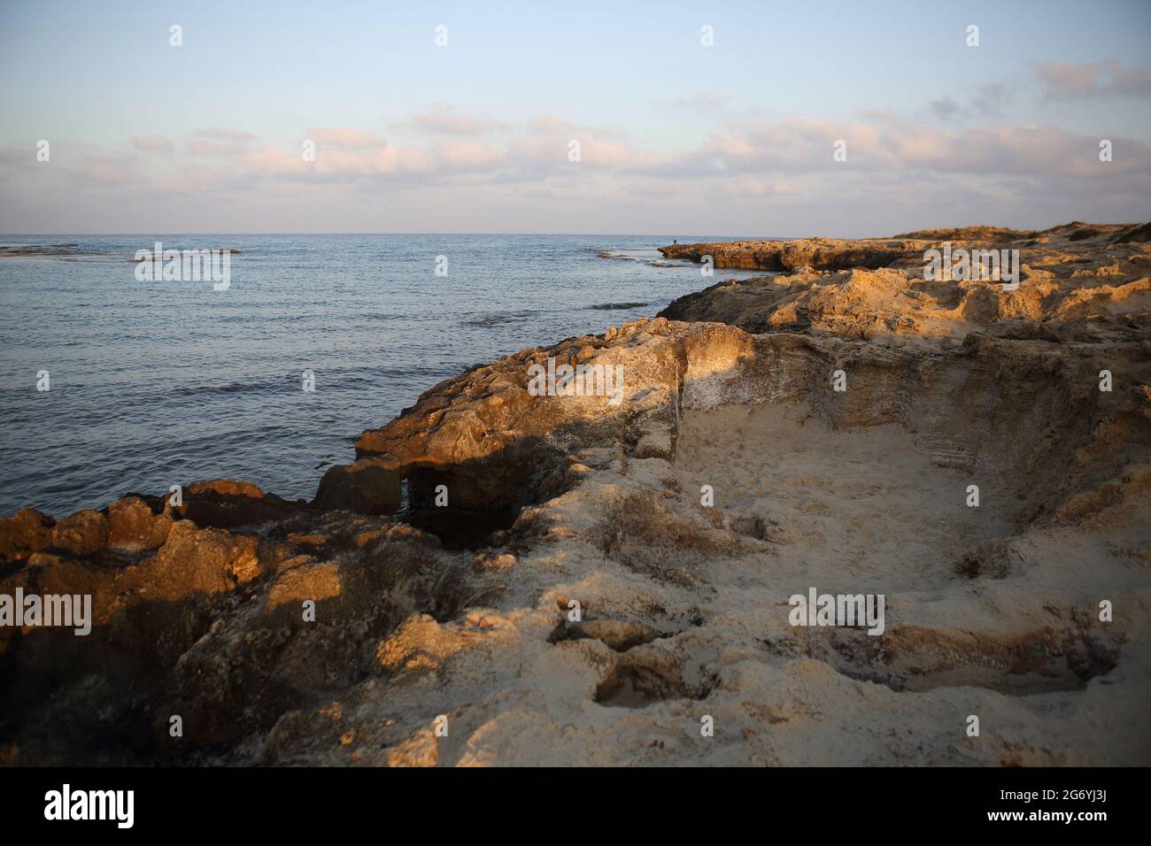 Ufer des Mittelmeers bei Sonnenaufgang, Sandsteinfelsen, Wellen oder Wellenschlag, Reflexionen und Wolken am dramatischen Himmel über dem Mittelmeer. Stockfoto
