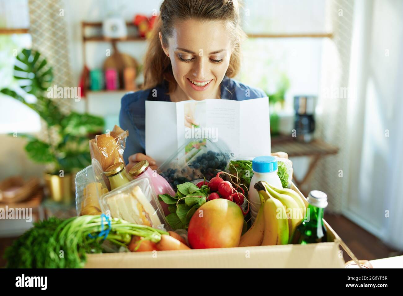 Lächelnde Hausfrau mittleren Alters mit Food-Box und Rezepte Liste in der Küche. Stockfoto