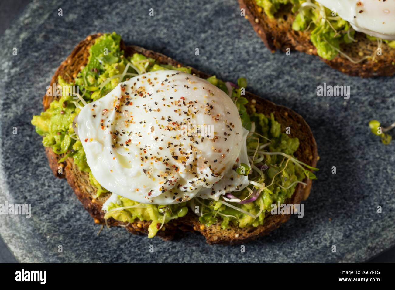 Hausgemachter gesunder Avocado-Toast mit pochiertem Ei und Sprossen Stockfoto