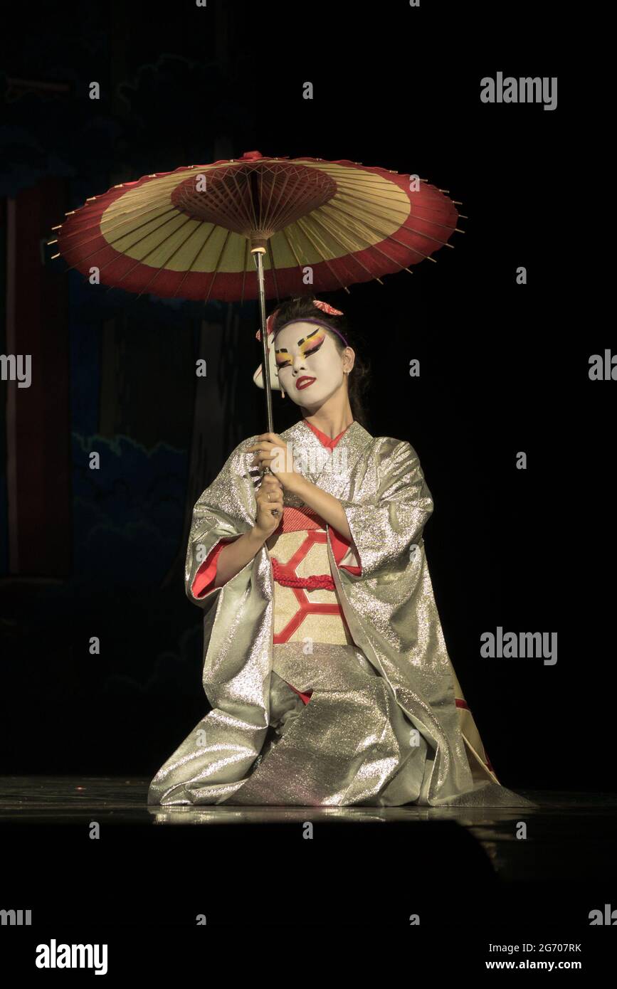 Japanische Frau in traditionellem Kimono mit Regenschirm auf den Knien Stockfoto