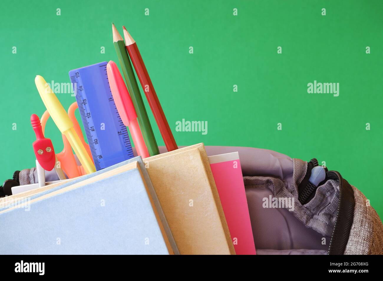Schulrucksack, Bücher, Notizbuch, Schreibwaren, grüner Hintergrund. Stockfoto
