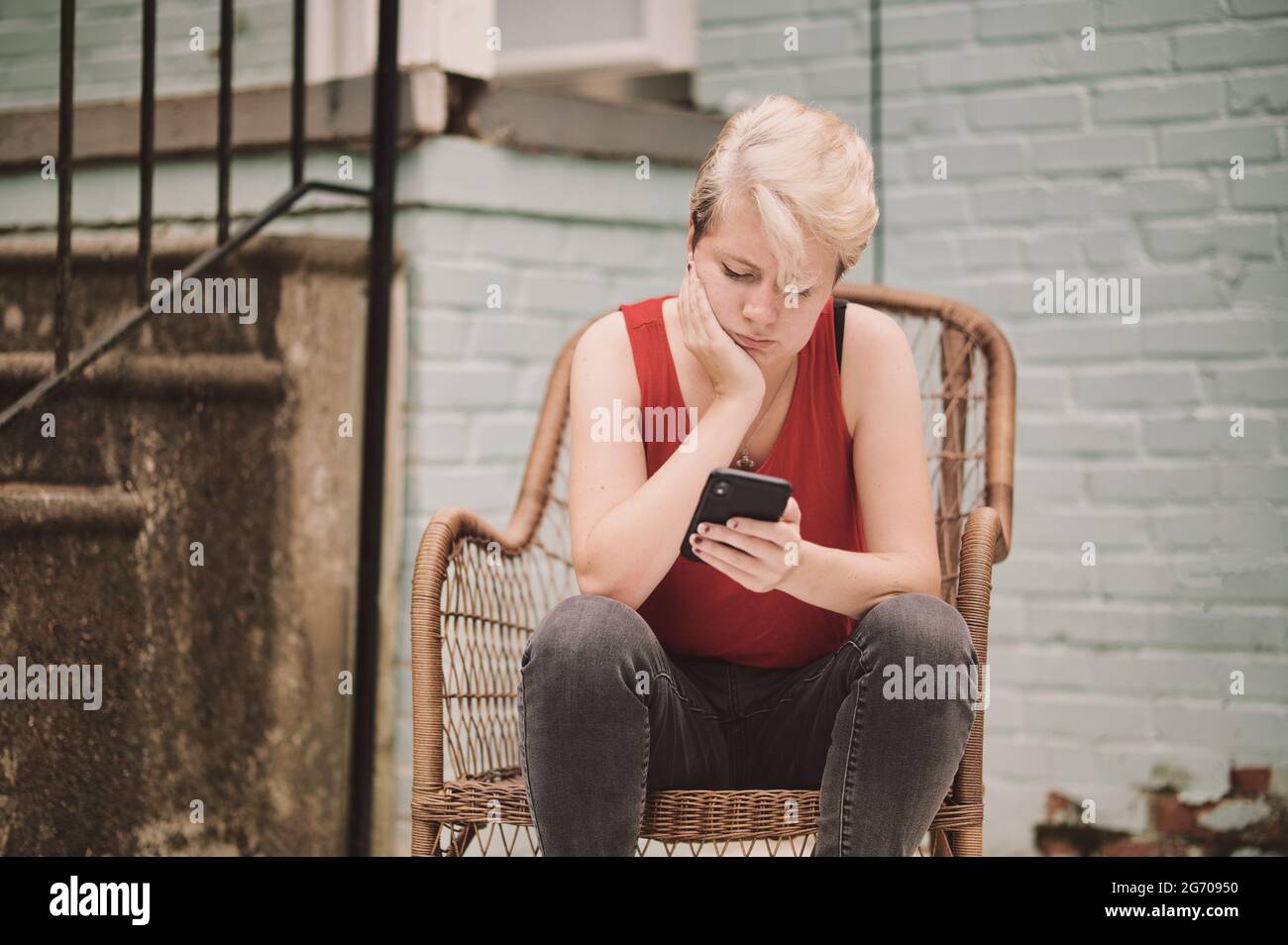 Junge Person, die auf dem Stuhl sitzend auf das Handy schaut Stockfoto
