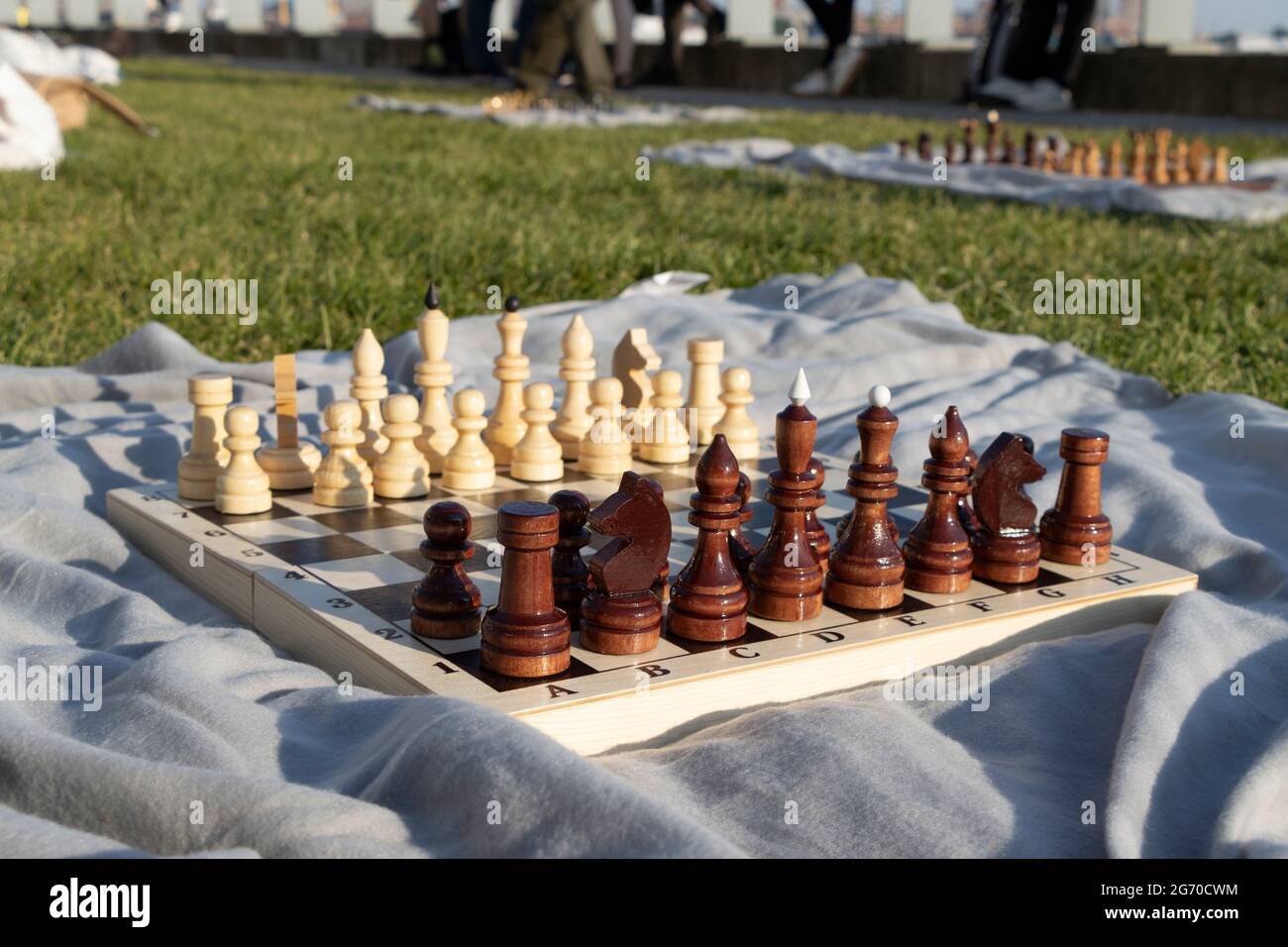 Ein hölzernes Schachbrett mit Figuren in einem Park auf einer grauen Decke. Amateur-Schachturnier im Park auf dem grünen Gras. Stockfoto