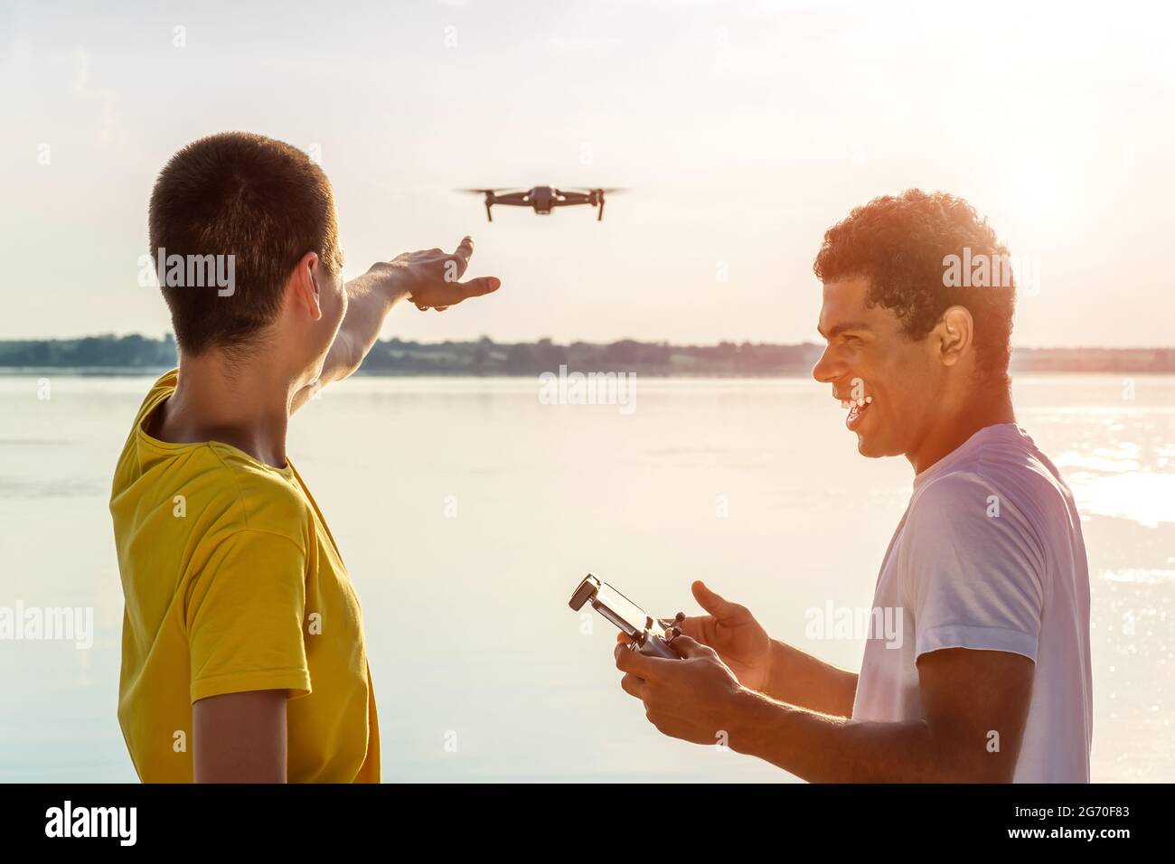 Zwei junge Blogger bedienen Drohne mit Controller in der Nähe des Flusses Stockfoto