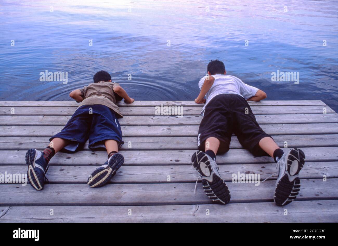 Zwei junge Jungen liegen auf einem Steg und blicken ins Wasser des Kawawaymog Lake, Algonquin, Ontario, Kanada. Stockfoto