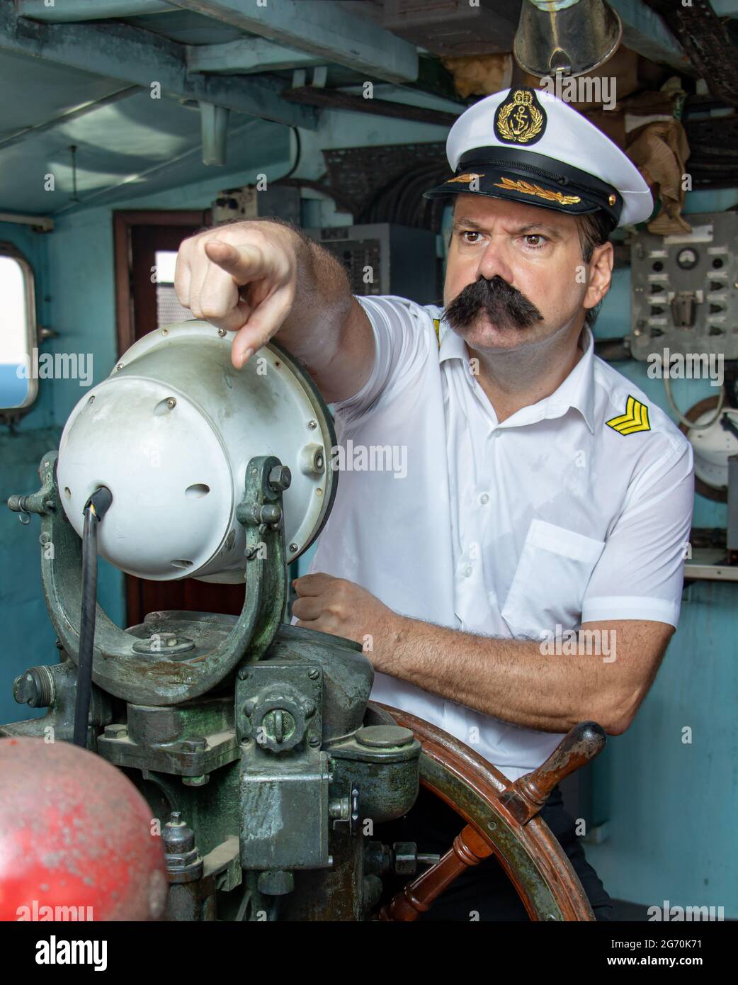 Ein Seemann-Offizier in der Uniform steuert das Schiff mit einem Ruder. Kapitän im Steuerhaus zeigt mit dem Finger nach vorne. Stockfoto