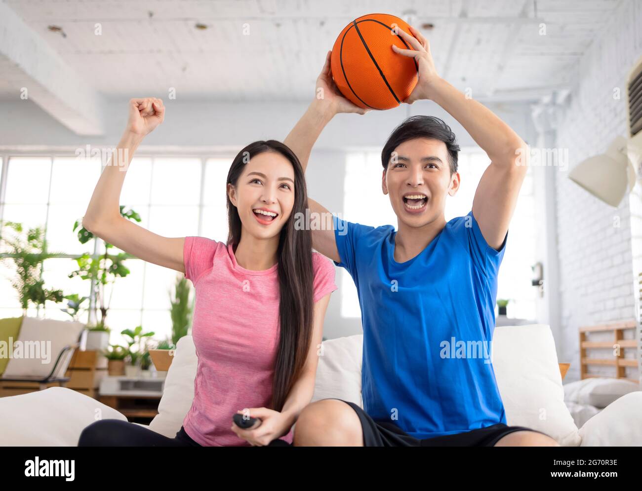 Junges Paar, das Fernsehen schaut und die Hände hebt, um den Sieg zu feiern Stockfoto
