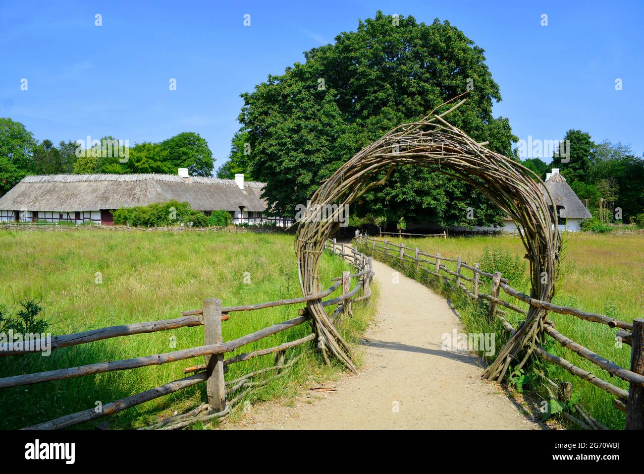 Lyngby, Dänemark - Juli 2021: Hölzerner Torbogen am Eingang des alten Dänemarks, Freilichtmuseum (Frilandsmuseet) mit alten Gebäuden im Hintergrund. Stockfoto