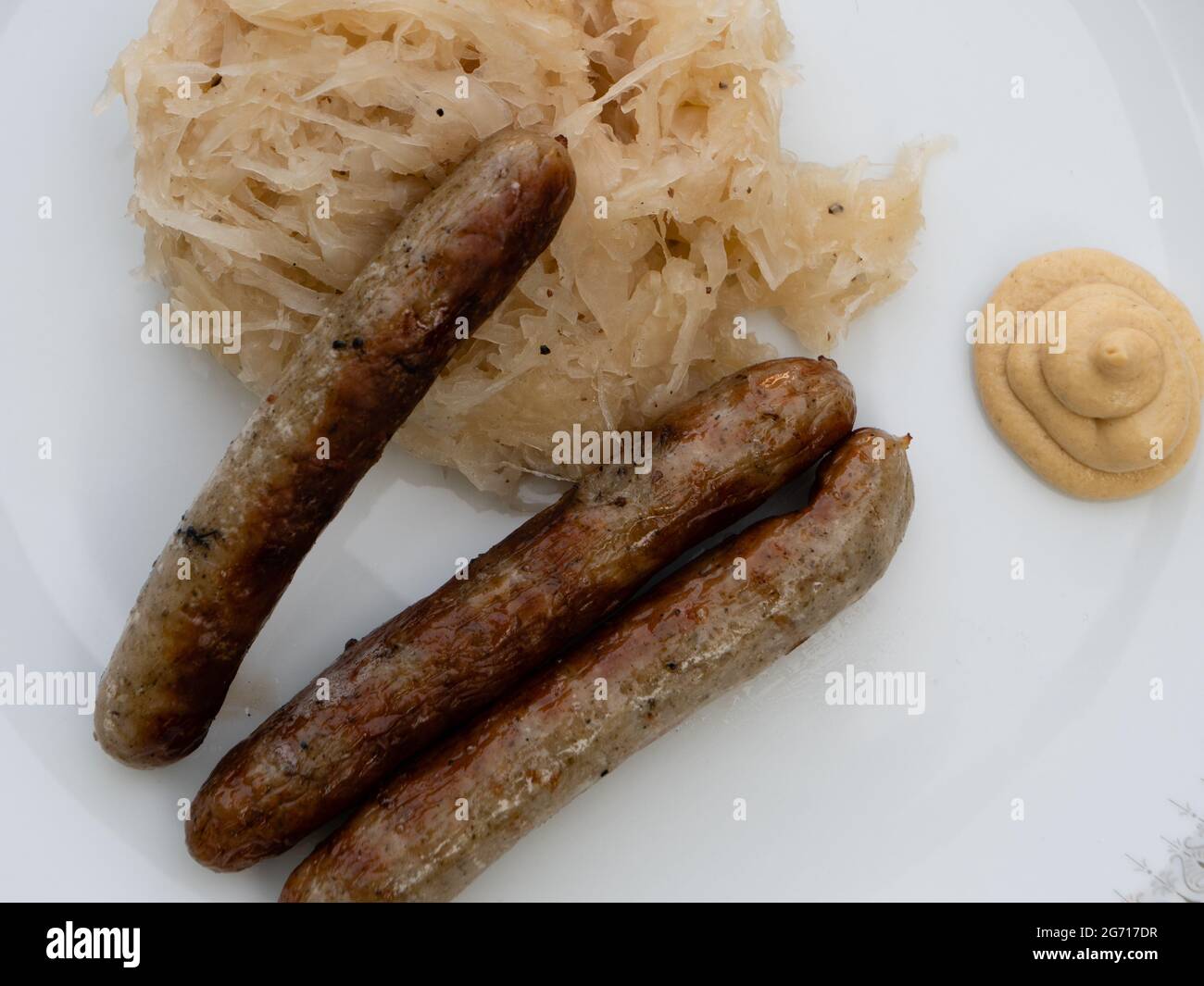 Nürnberger Grillwurst oder Nürnberger Rostbratwurst mit Sauerkraut oder saurem Kohl und Senf auf einem weißen Teller aus nächster Nähe Stockfoto