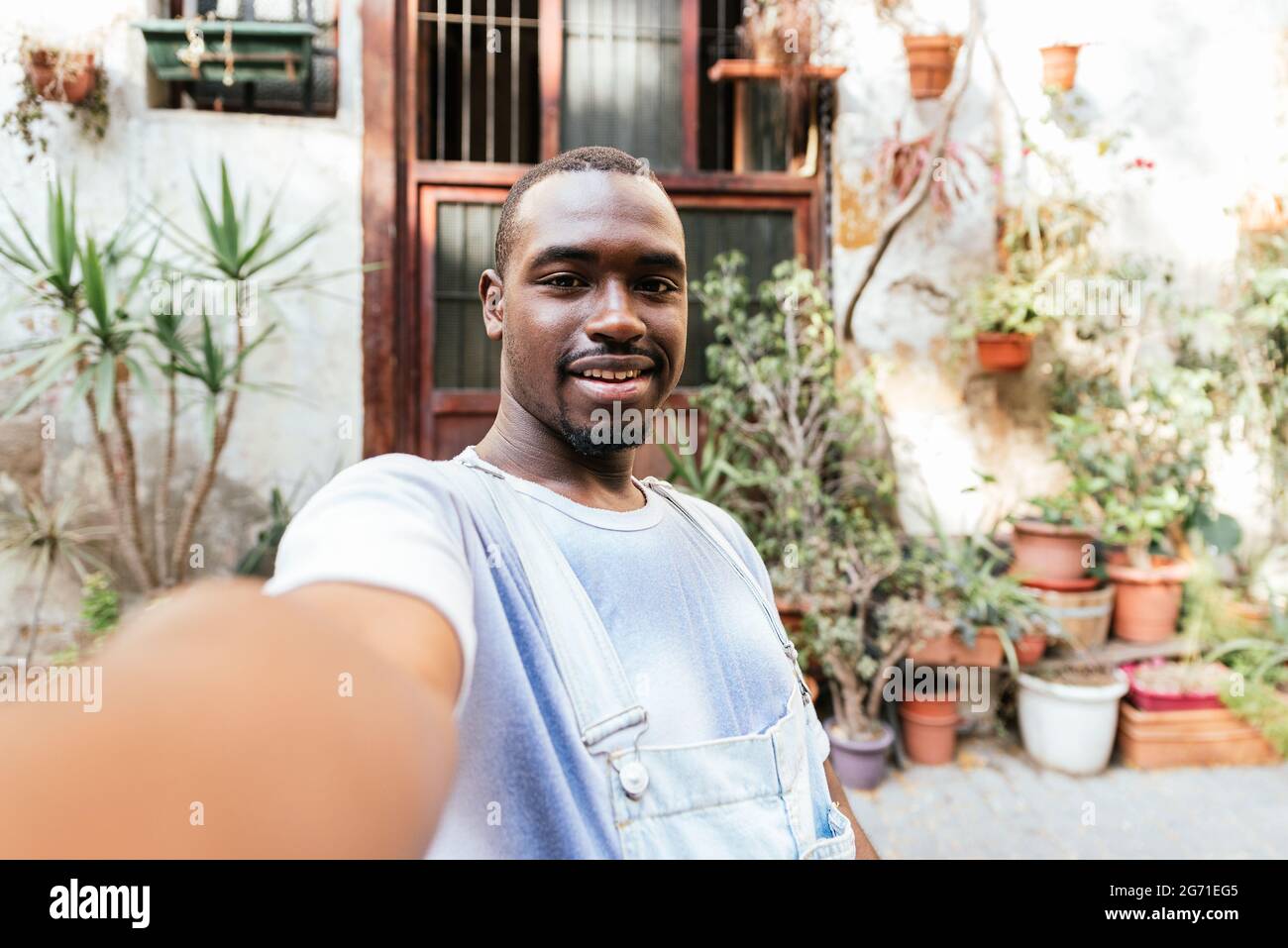 afrikanischer attraktiver Mann, der seinen Arm mit seinem Telefon hob, um ein Selfie zu machen. Er lächelt zur Kamera. Stockfoto