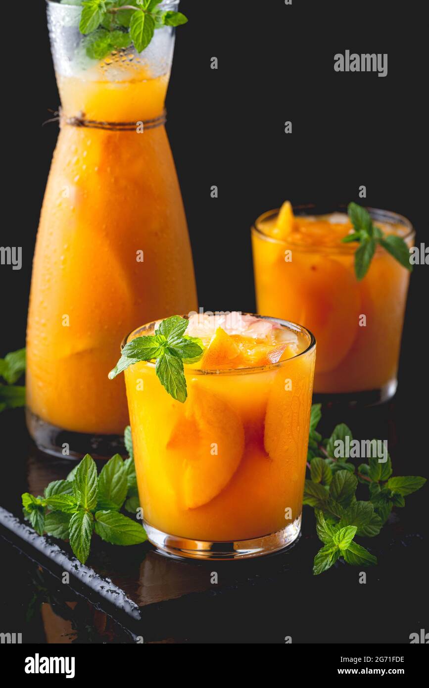 Kalte Getränke im Sommer: Hausgemachte Pfirsich-Sangria mit Eis und Minze im Glas auf schwarzem Hintergrund. Stockfoto