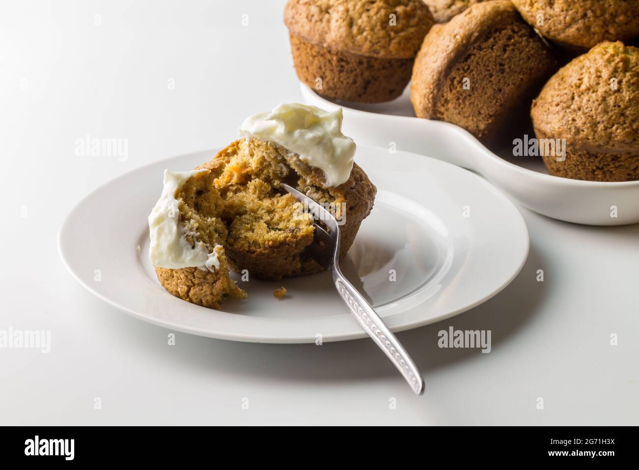 Muffin mit Karotten-Zimt-Kuchen und Joghurt auf weißem Servierteller mit Muffins im Hintergrund isoliert auf weiß mit Platz zum Kopieren - Nahaufnahme Stockfoto