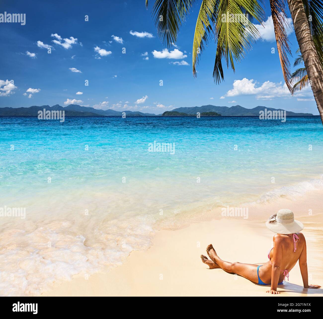 Wunderschöner tropischer Strand mit klarem Wasser und weißem Sand, Frau nimmt Sonnenbaden unter der Palme Stockfoto