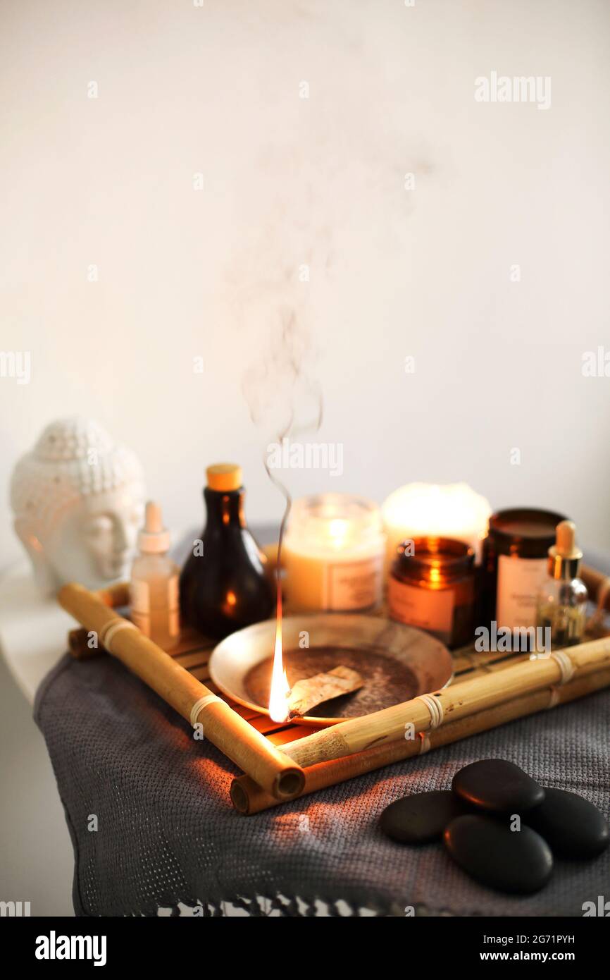Aromatischer Räucherstäbchen, der auf einem Bambustablett in der Nähe von Aromatherapie-Vorräten vor weißem Hintergrund brennt Stockfoto