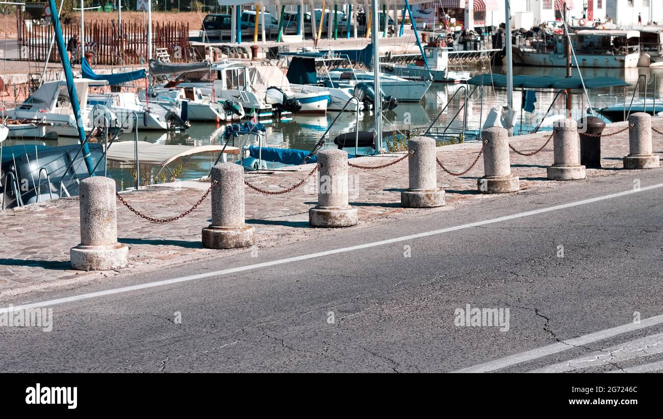 Betonbollard mit rostigen Ketten am Hafen auf der Anlegestelle vor Booten (Marken, Italien, Europa) Stockfoto