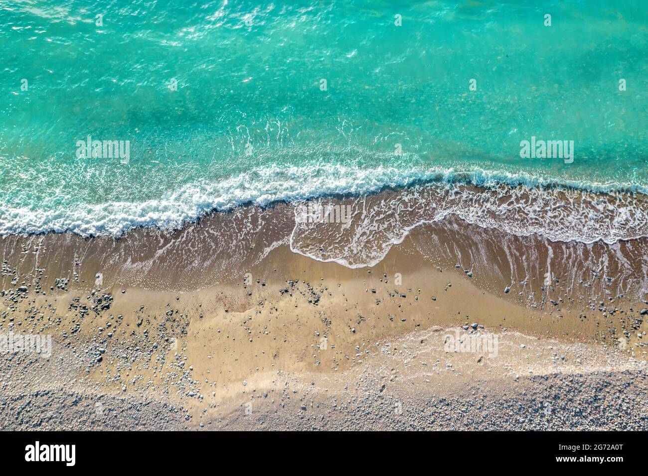 Meereswellen brechen an einem wilden Strand mit Sand und Kieselsteinen, dröhnen aus der Sicht von direkt oben Stockfoto