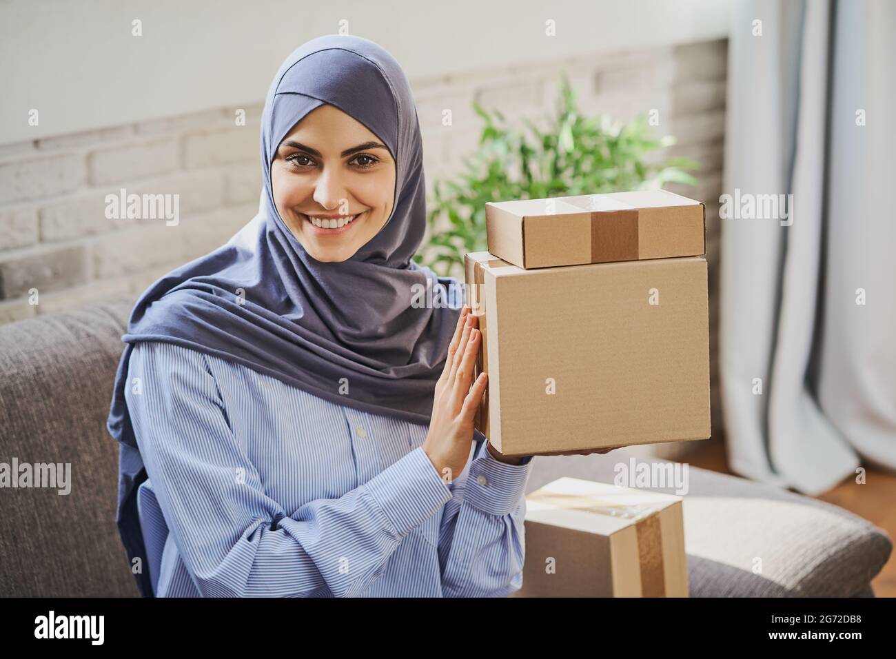 Eine hübsche arabische Frau, die ein paar Kartons hält und ein breites Lächeln auf den Lippen zaubert Stockfoto