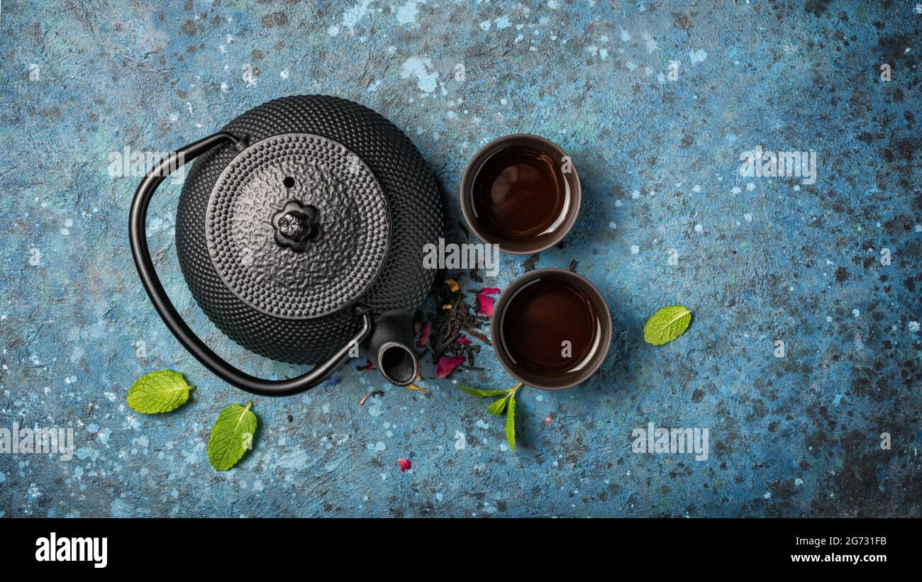 Draufsicht auf schwarze japanische gusseiserne Teekannen und Tee mit grünen Minzblättern auf blauem Betonhintergrund mit Kopierraum Stockfoto
