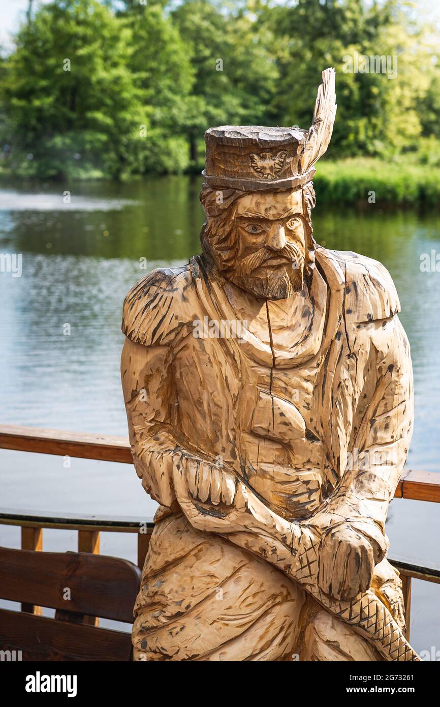 Zwierzyniec, Lubelskie, Polen - 02. Juli 2021: Holzskulptur eines traditionell gekleideten Mannes; schöner Teich im Hintergrund. Stockfoto