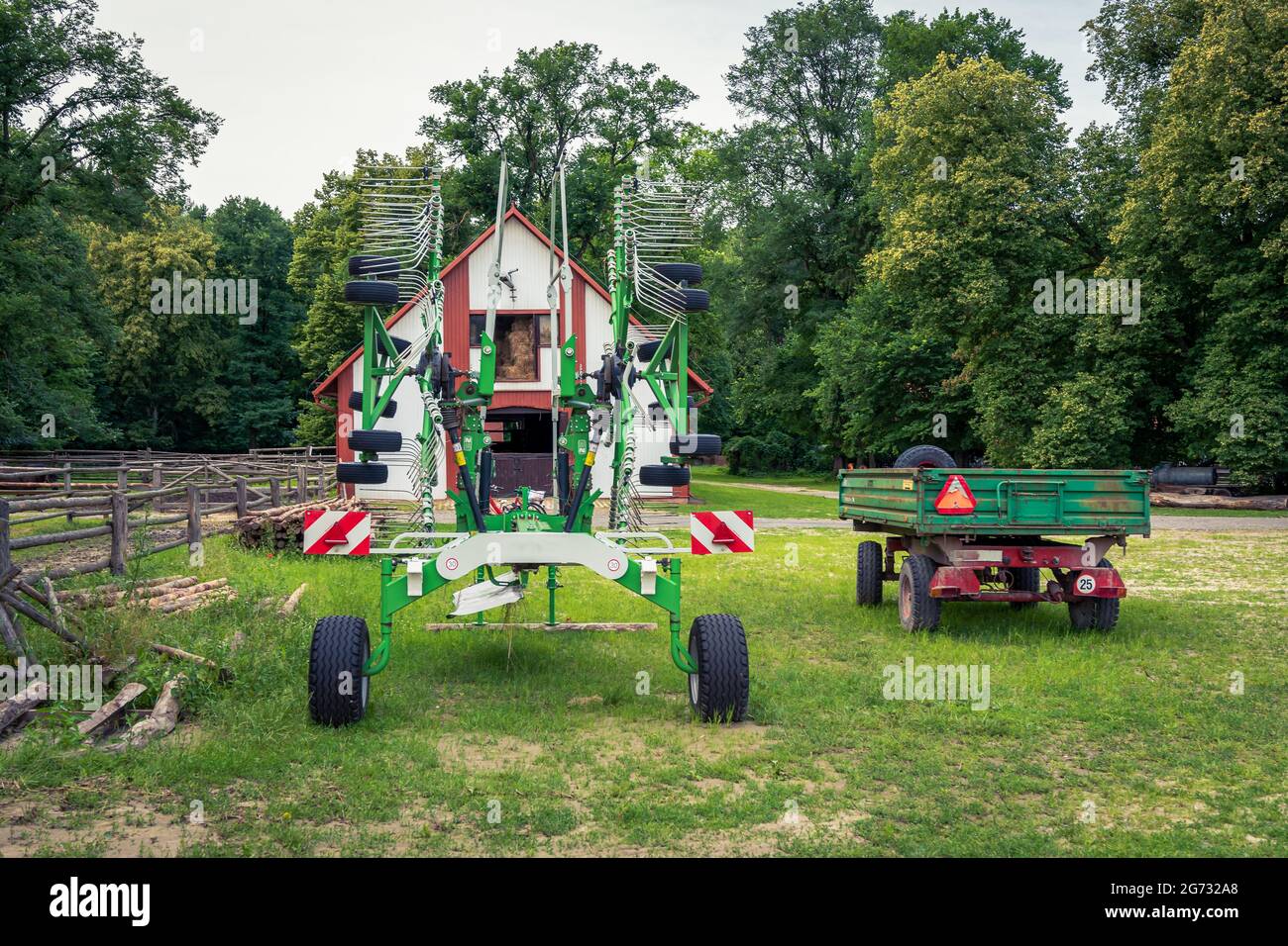 Gebrauchte, bunte landwirtschaftliche Geräte stehen auf einem Bauernhof, umgeben von Bäumen an einem sonnigen Tag Stockfoto