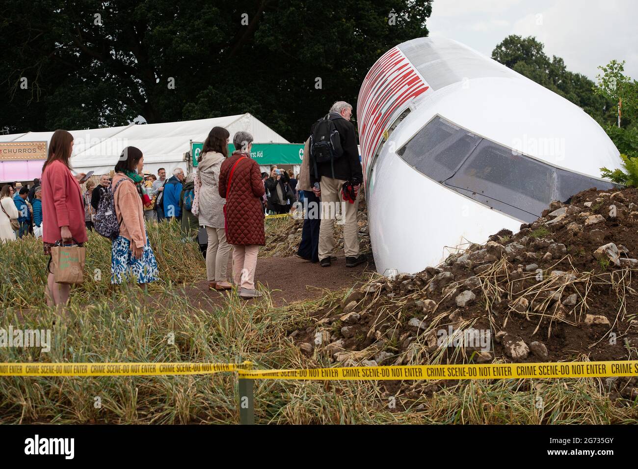 East Molesey, Surrey, Großbritannien. Juli 2021. Die Menschen stehen Schlange, um den sehr beliebten Global Impact Garden, Extinction von Designr Felecity O'Rourke, zu sehen. Es war ein sehr geschäftiger Tag heute am 4. Tag des RHS Hampton Court Palace Garden Festivals. Im echten britischen Stil schien die Sonne am Morgen, aber am Nachmittag folgten heftige Duschen, da Sonnenschirme und Ponchos die Accessoires waren, die man unbedingt haben sollte. Quelle: Maureen McLean/Alamy Stockfoto