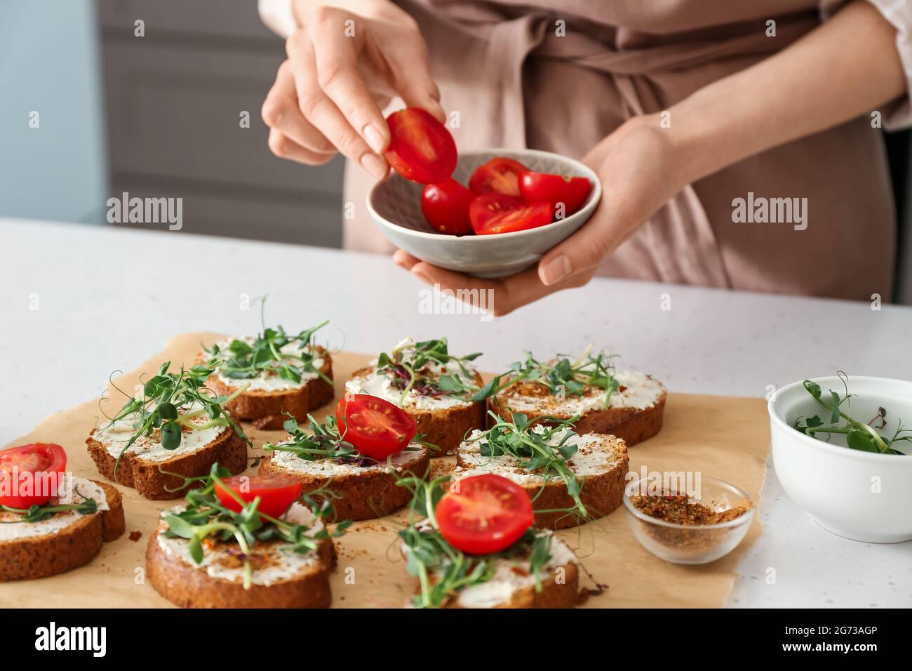 Weibliche Köchin, die Tomatenkirsche zum Toasten auf dem Küchentisch hinzufügte, Nahaufnahme Stockfoto
