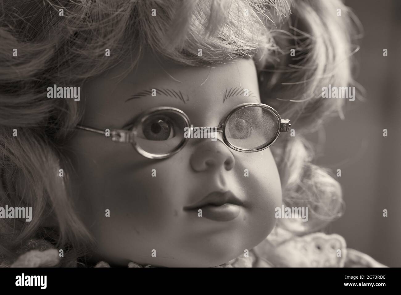 Porträt einer Vintage-Puppe, eines Spielzeugmädchen mit blondem Haar und Brille. Stockfoto