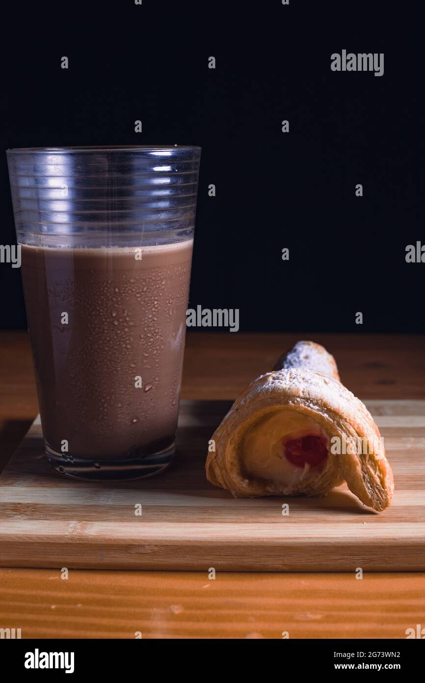 Eine leckere kegelförmige Süßigkeit und ein Glas Schokolade auf einem Holzbrett auf dem Tisch Stockfoto