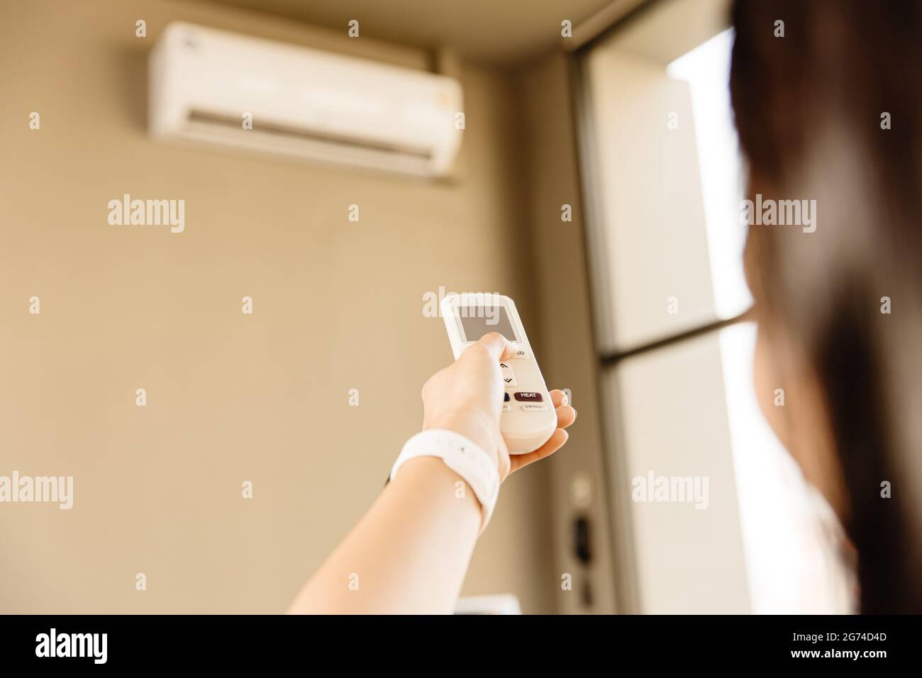 Nahaufnahme Personen mit Fernbedienung passen die Raumtemperatur im Heimbüro an und zeigen auf Klimaanlage in der heißen Sommersaison. Stockfoto
