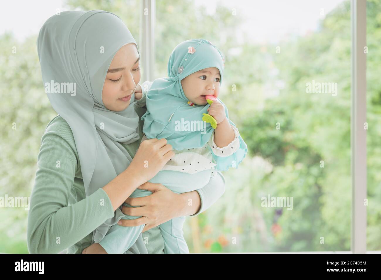 Muslimische Mutter mit ihrem Baby. Islamisch-asiatische Frauen tragen Hijab halten Unterstützung Kind Kleinkind innen zu Hause. Stockfoto