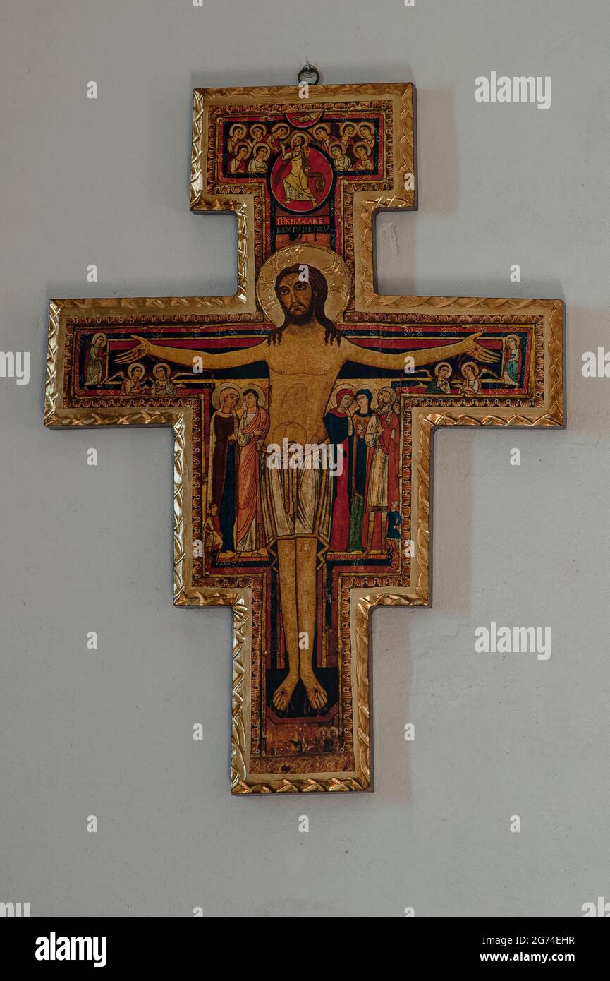 Spätmittelalterliches Kruzifix, gemalt auf Holz, Mitte der 1300er Jahre Chiesa oder Chiesetta di San Tommaso Apostolo (Kirche des Apostels Thomas) in Cavedago, Trentino-Südtirol, Italien. Vor einem Hintergrund aus Rot, Schwarz und Gold bewegen sich Engel unter den ausgestreckten Armen Christi, und sein Körper wird von den langen Figuren der Heiligen Maria, des Heiligen Johannes des Evangelisten und anderer Trauer flankiert. Stockfoto
