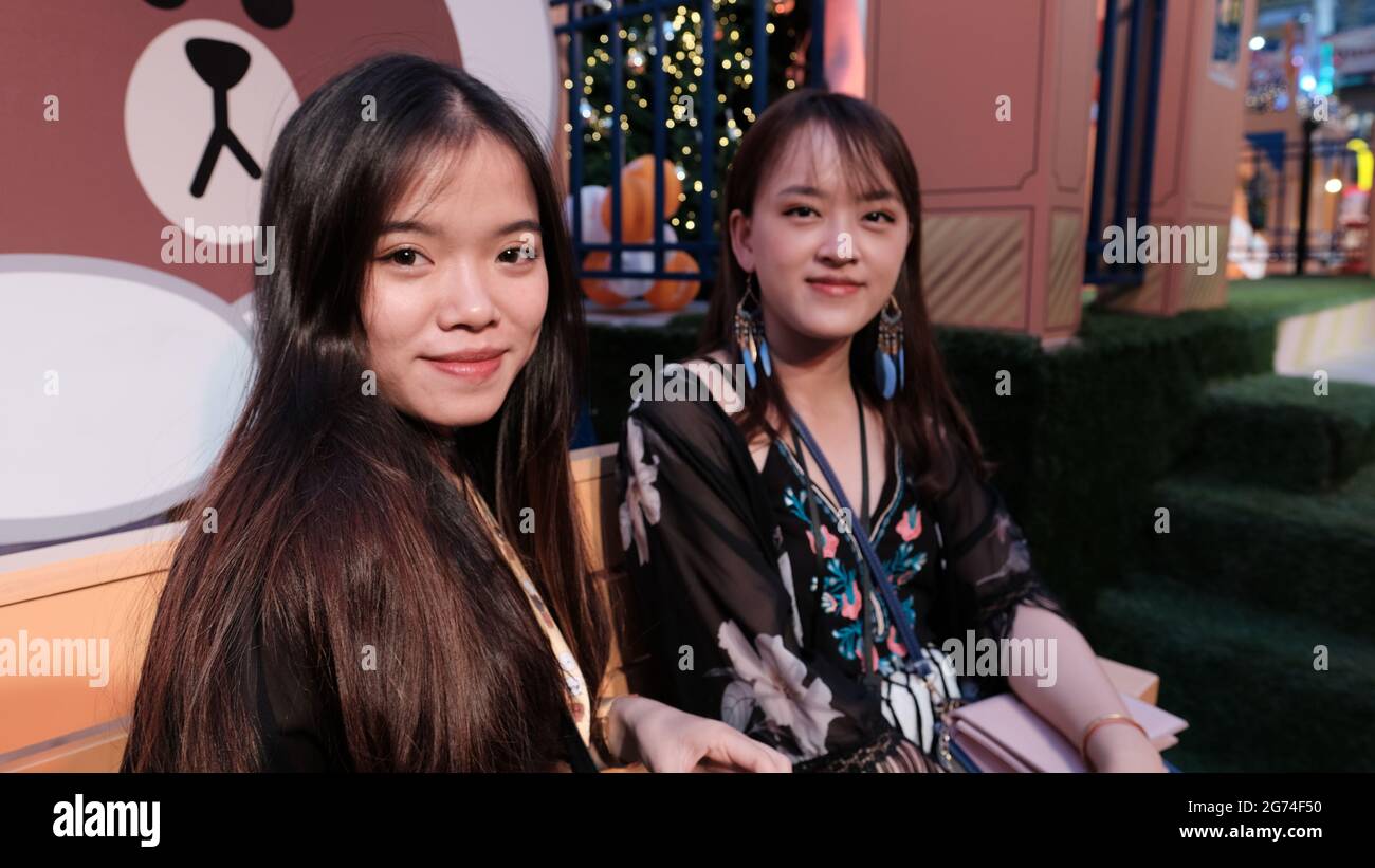 Zwei junge asiatische Touristen-Damen sitzen auf einer Bank und planen ihren Umzug im Zentrum von Bangkok, Thailand Stockfoto