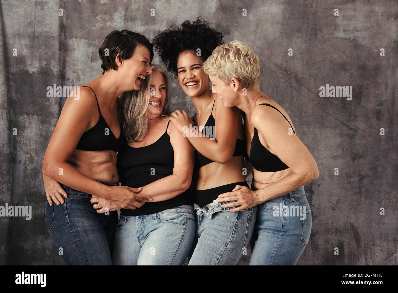 Schöne Frauen unterschiedlichen Alters lachen zusammen in einem Studio. Vier verschiedene und körperpositive Frauen feiern ihren natürlichen Körper, während sie J tragen Stockfoto