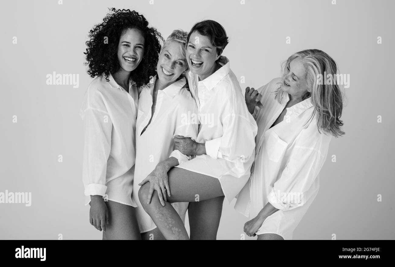 Schwarz-Weiß-Aufnahme verschiedener weiblicher Modelle, die ihre natürlichen Körper umarmen. Vier selbstbewusste und glückliche Frauen lächeln fröhlich, während sie weißen Sh tragen Stockfoto
